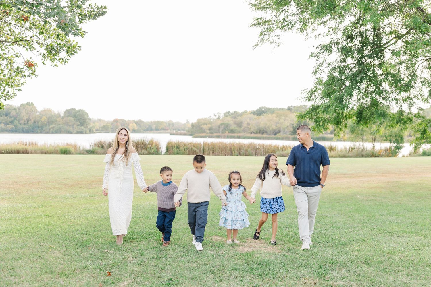 A series of outdoor family portraits in a grassy field with people wearing coordinated white and blue outfits. Busse Woods