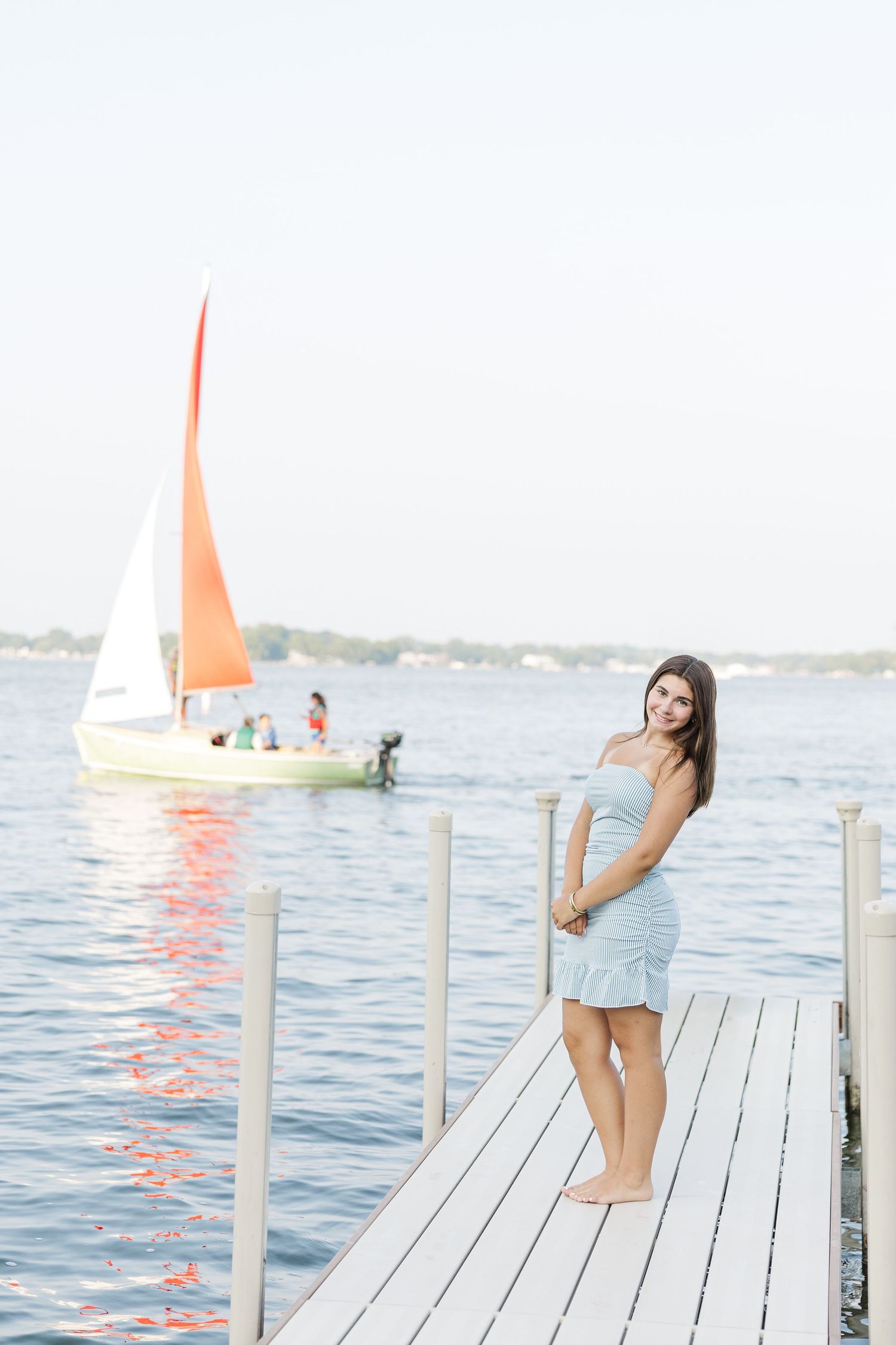 Teen girl on dock with red sailboat during Pistakee Lake family photos in Johnsburg, Illinois