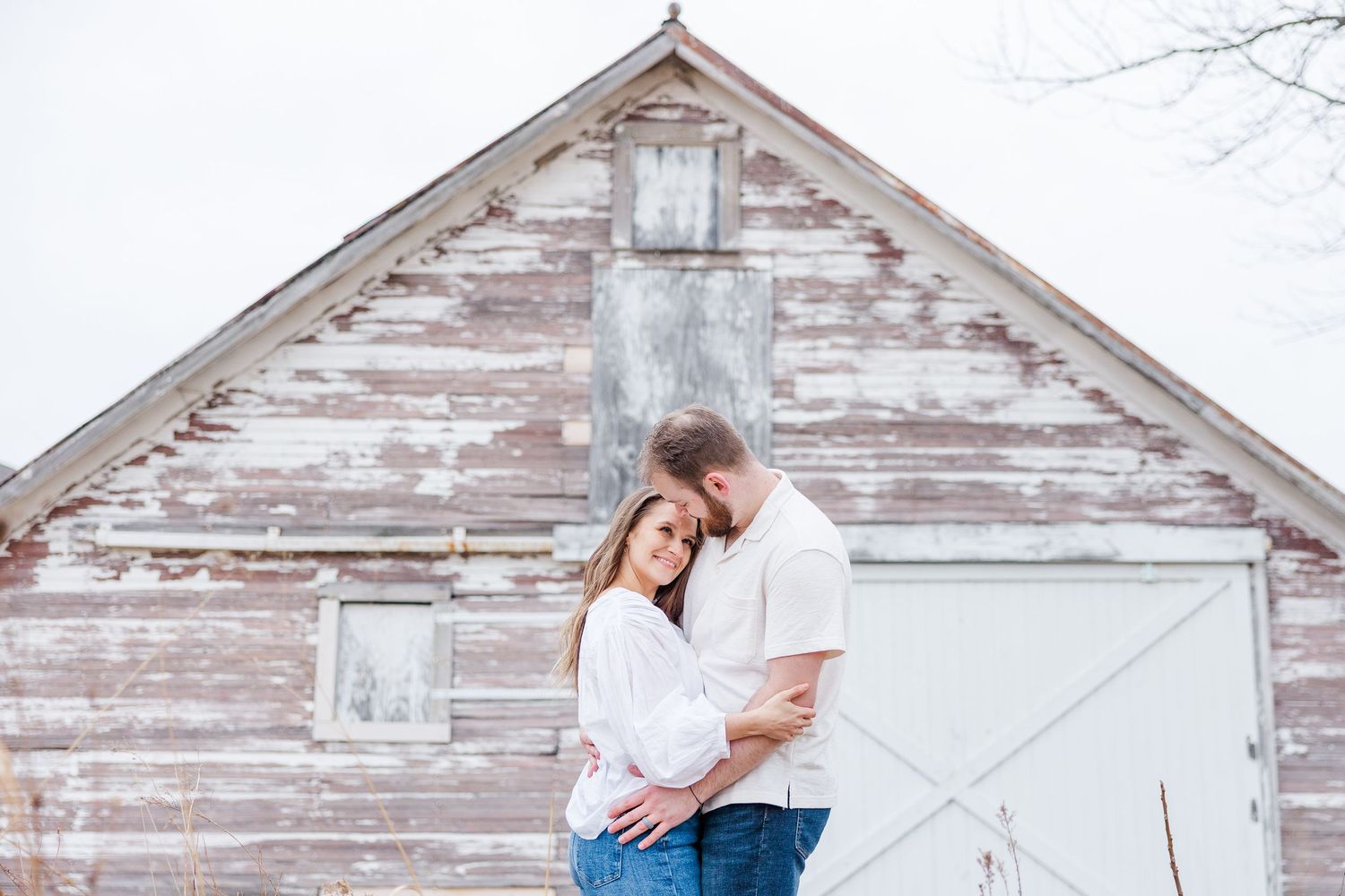Couple embracing in front of rustic barn during pregnancy announcement photos in Cary, Illinois