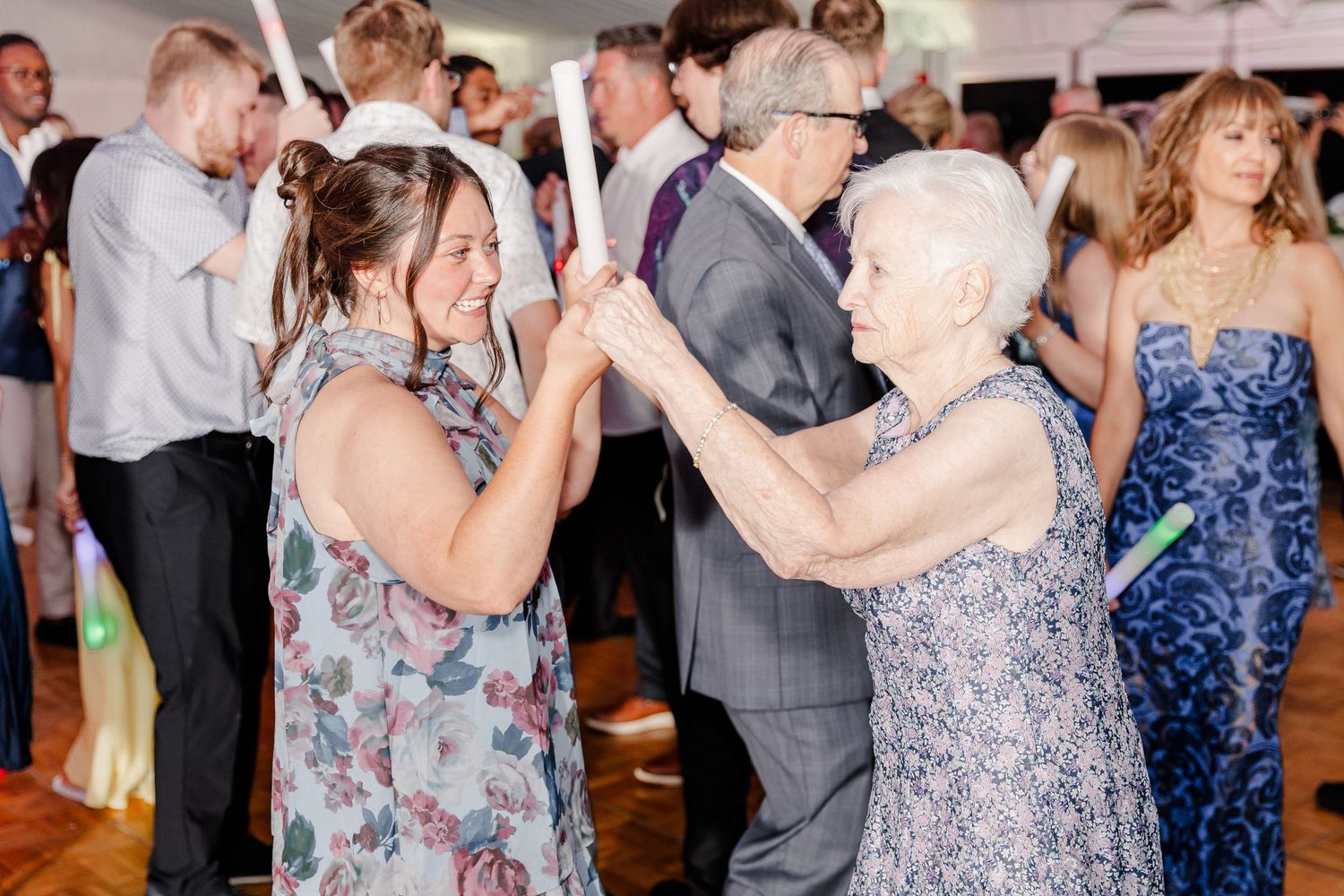 Two women dance joyfully with glow sticks at a lively wedding reception celebration.