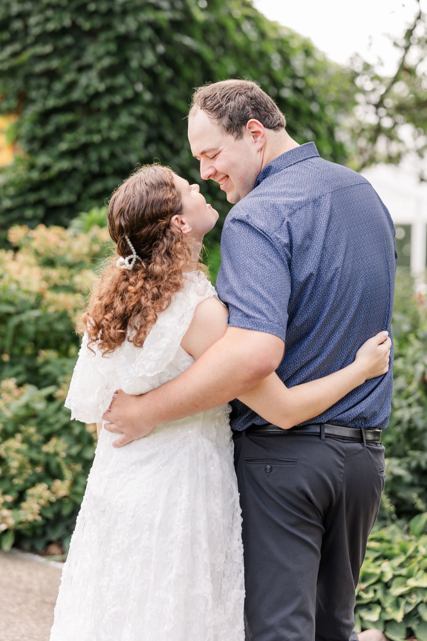 Couple embracing and smiling at each other in a lush green garden during an outdoor engagement session.