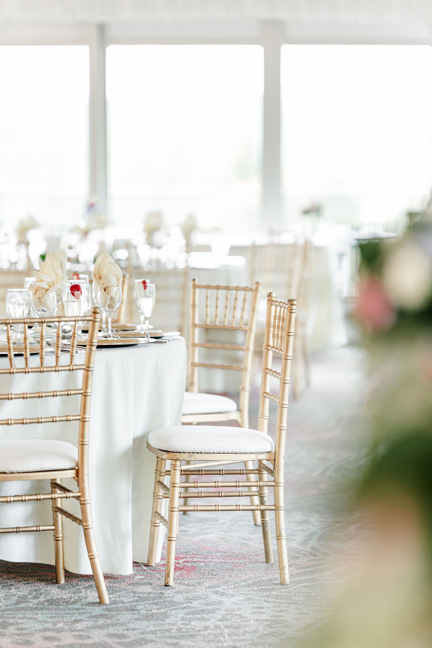 Gold chiavari chairs arranged at white linen tables in bright wedding reception venue.