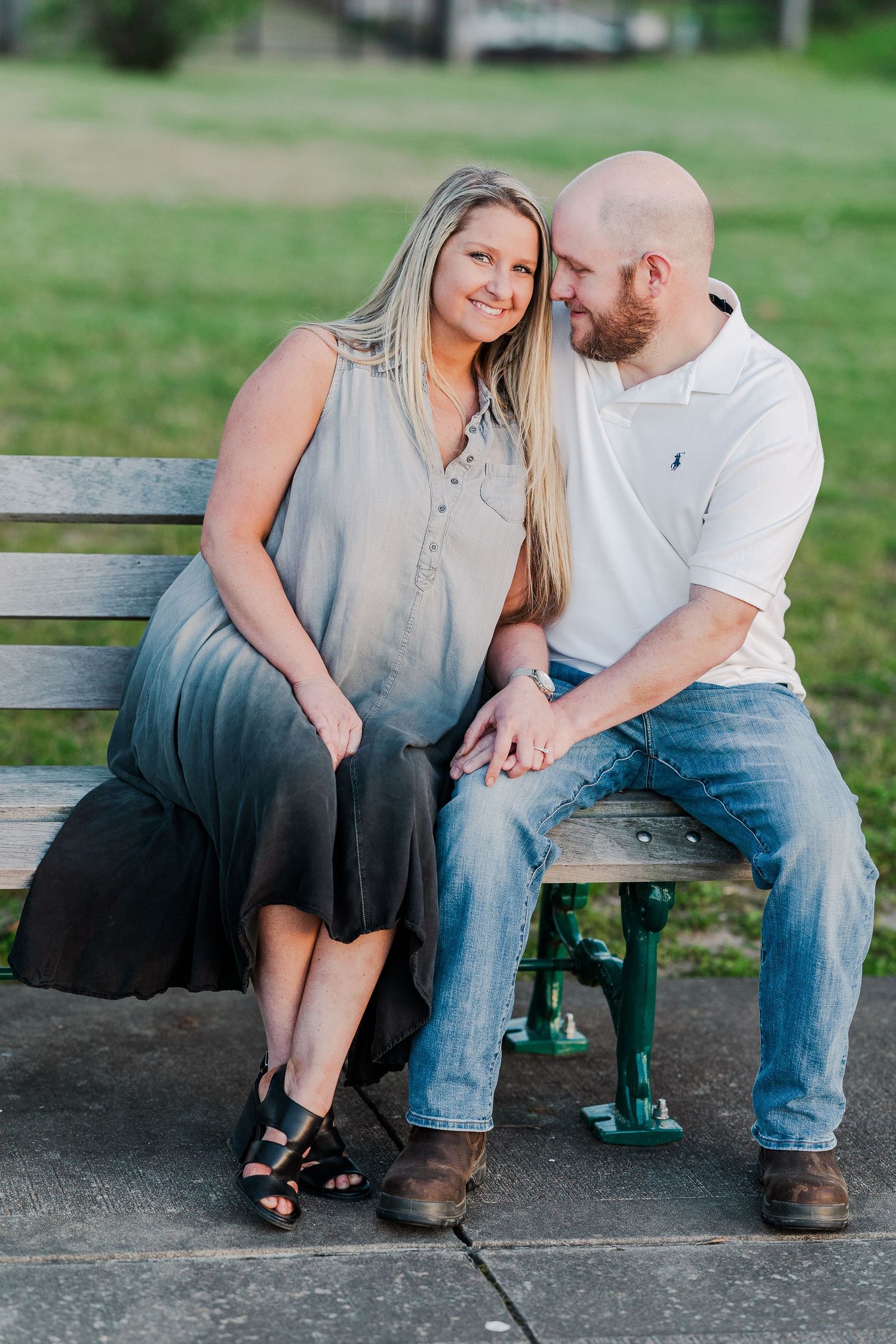 A couple sits close together on a green park bench sharing a tender moment.