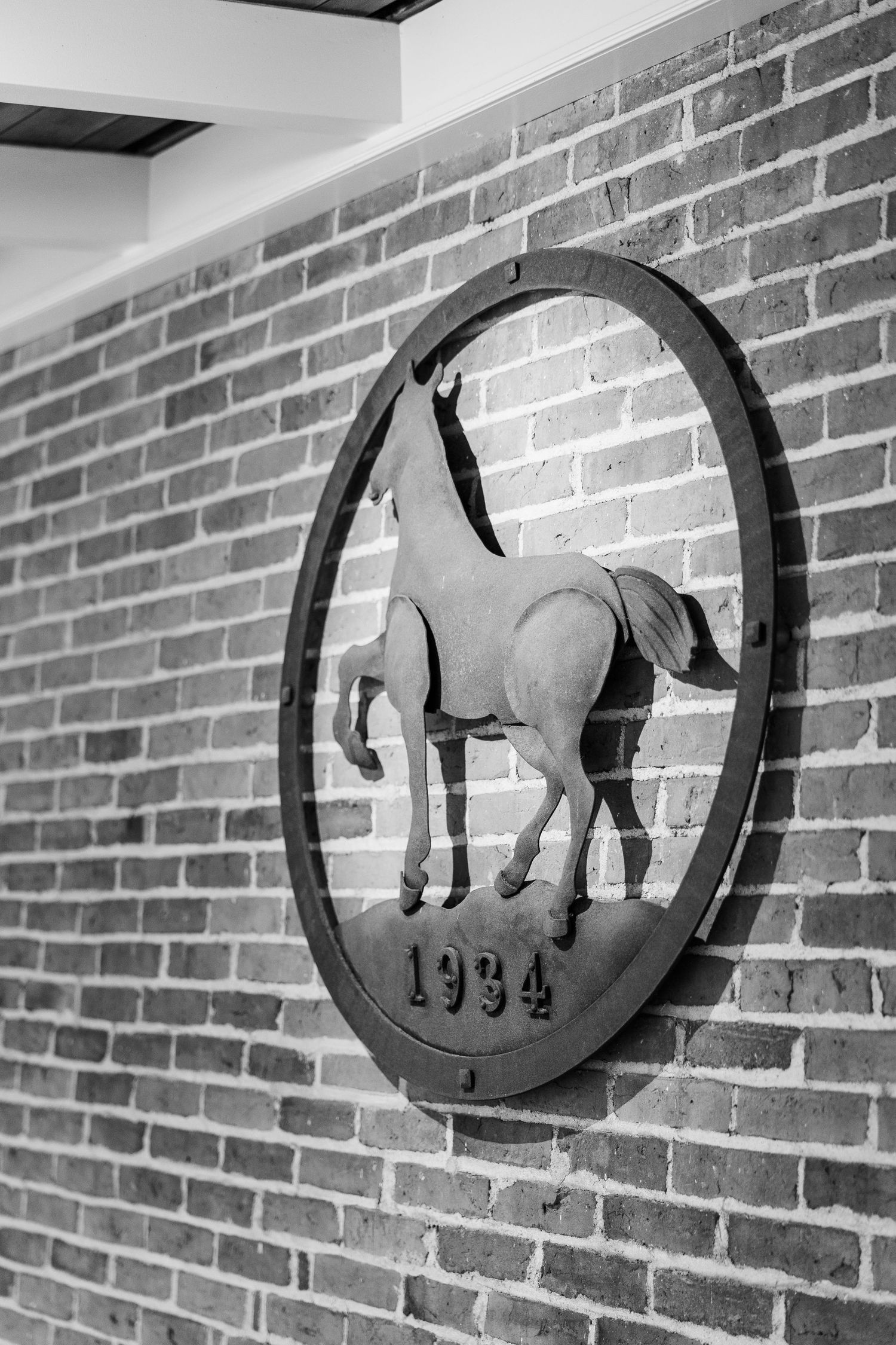 Black metal horse medallion dated 1994 mounted on brick wall.