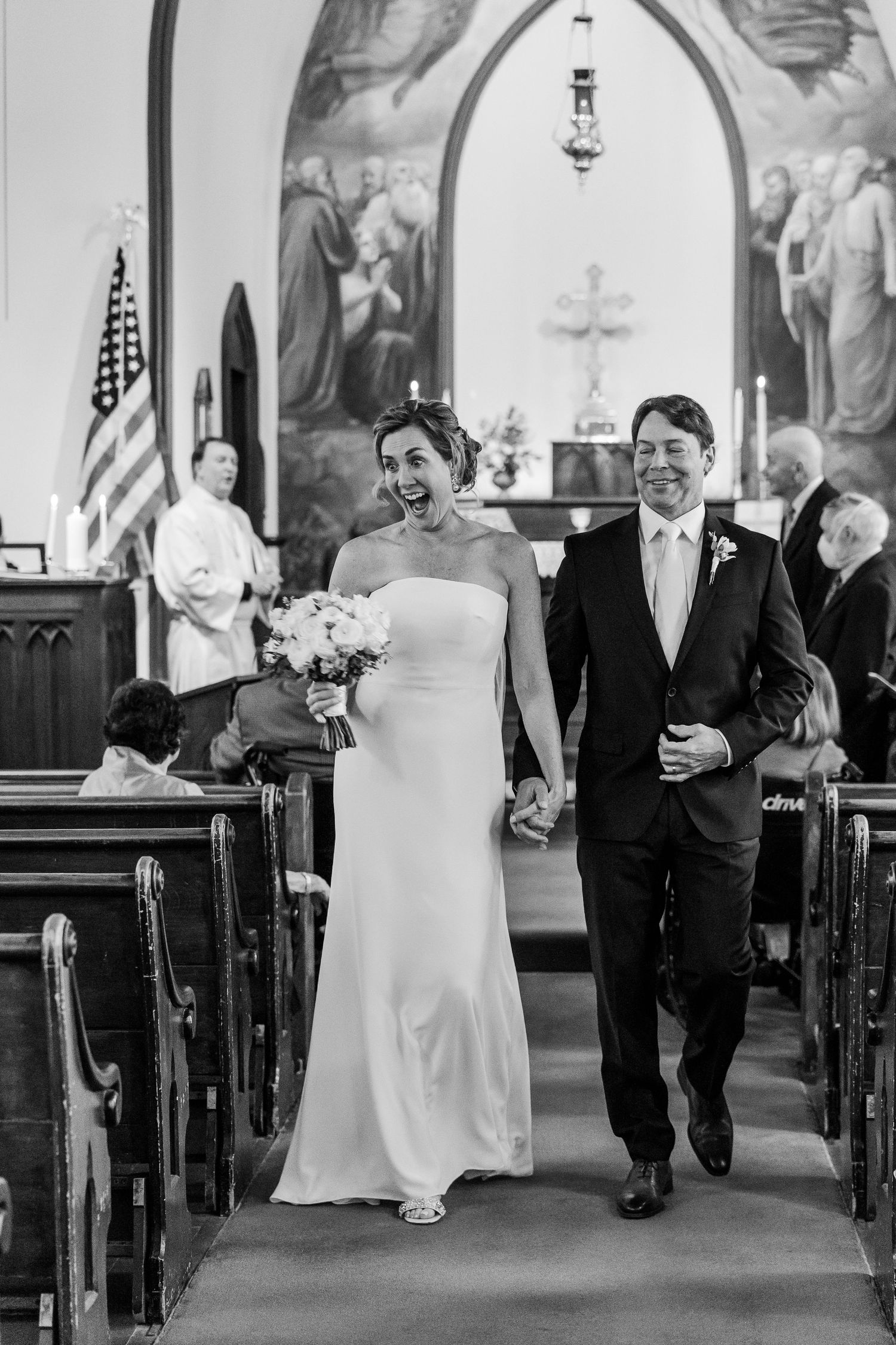 Black and white photo of joyful recessional down church aisle after wedding ceremony.