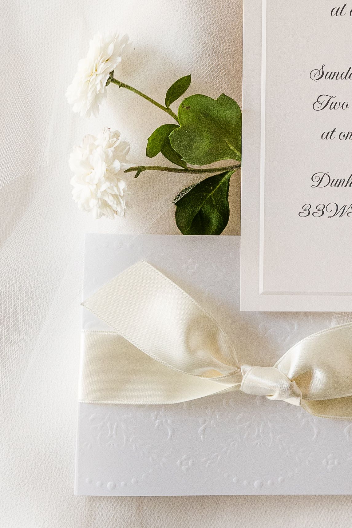 Wedding invitation detail showing white bow and fresh white flowers.