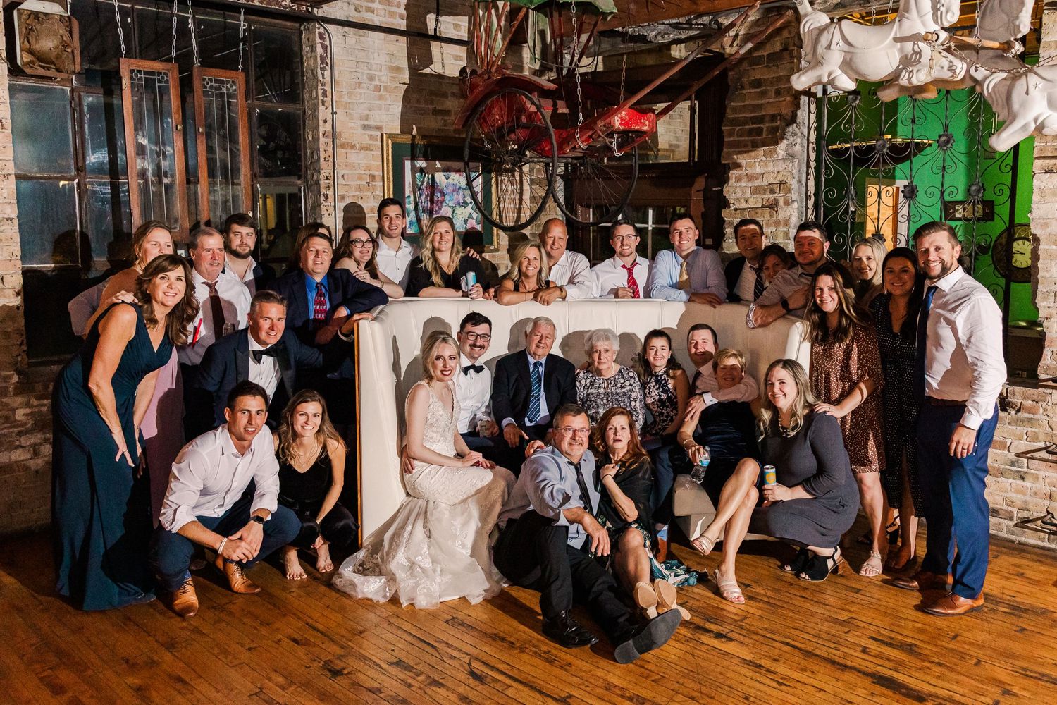 Large group photo of wedding party and guests posing together in an industrial-style venue.