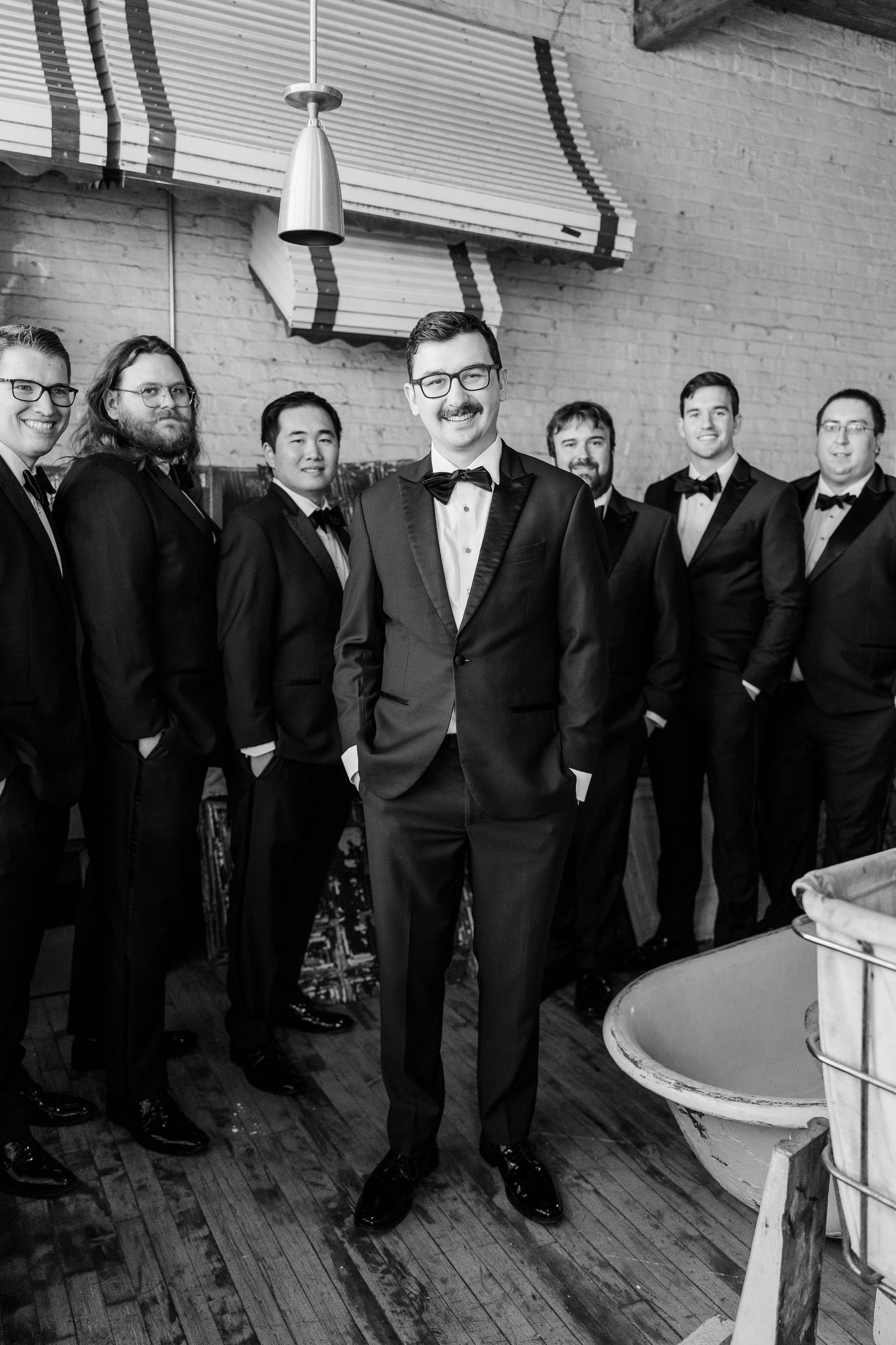 A black and white photo of a wedding party in tuxedos standing in a vintage room.