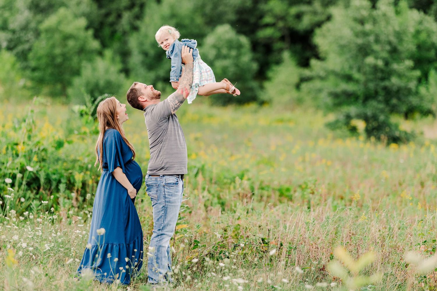 A joyful family moment in a wildflower meadow with lifted child against blue sky.