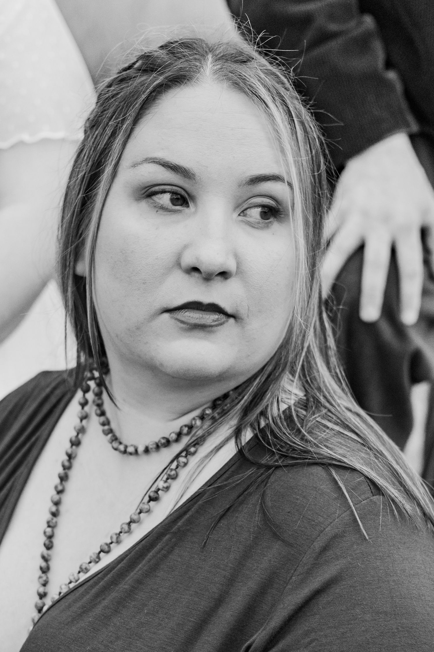 Black and white portrait of a wedding guest wearing dark clothing and beaded necklace.
