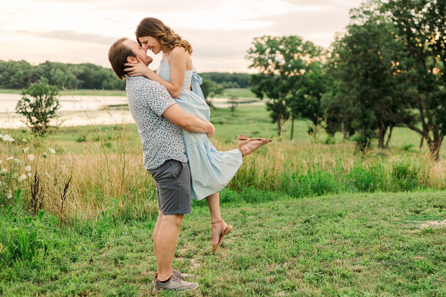 A couple enjoys a playful moment together in a grassy field at sunset.