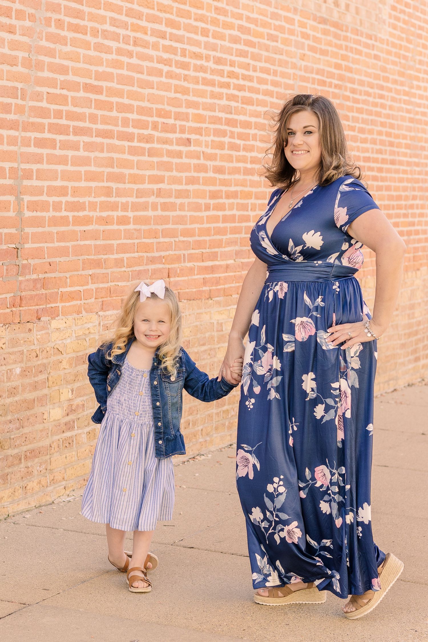 Two people in coordinating blue outfits pose together against a brick wall background.