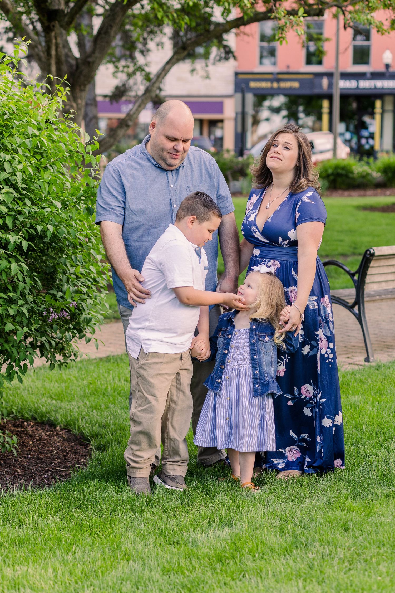 A family shares a sweet moment together on a grassy lawn near historic buildings.