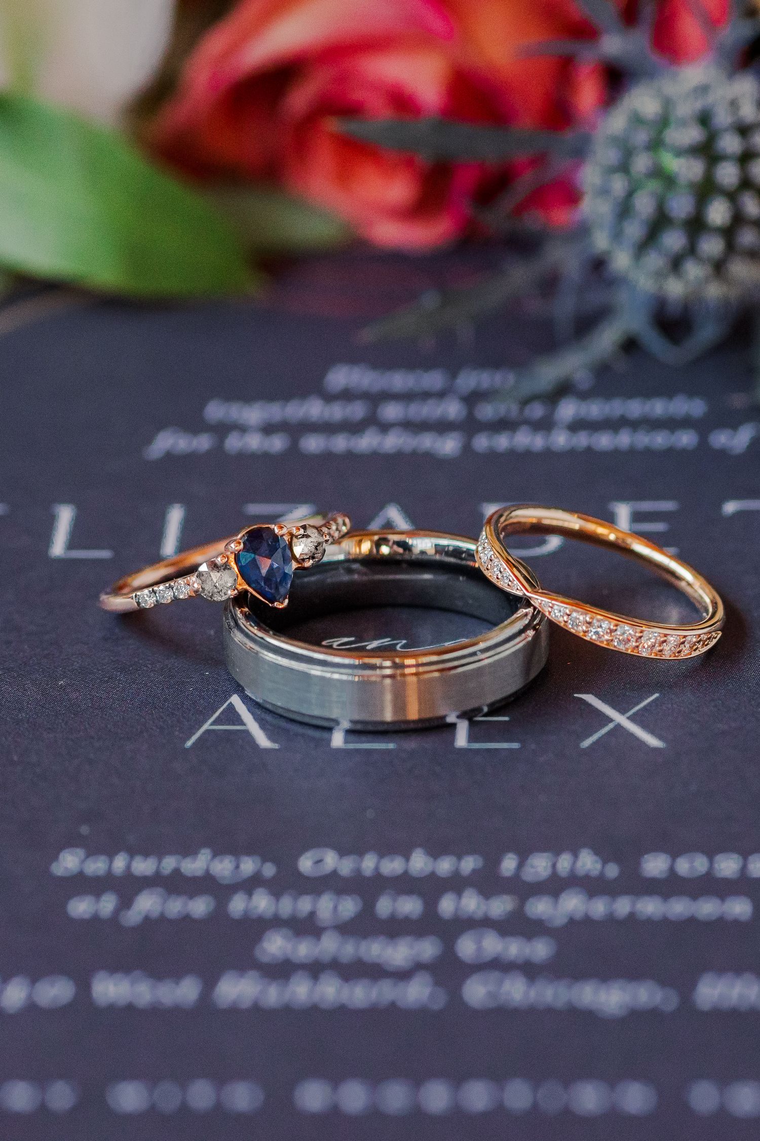 Three wedding rings including a sapphire engagement ring displayed on a navy blue invitation.