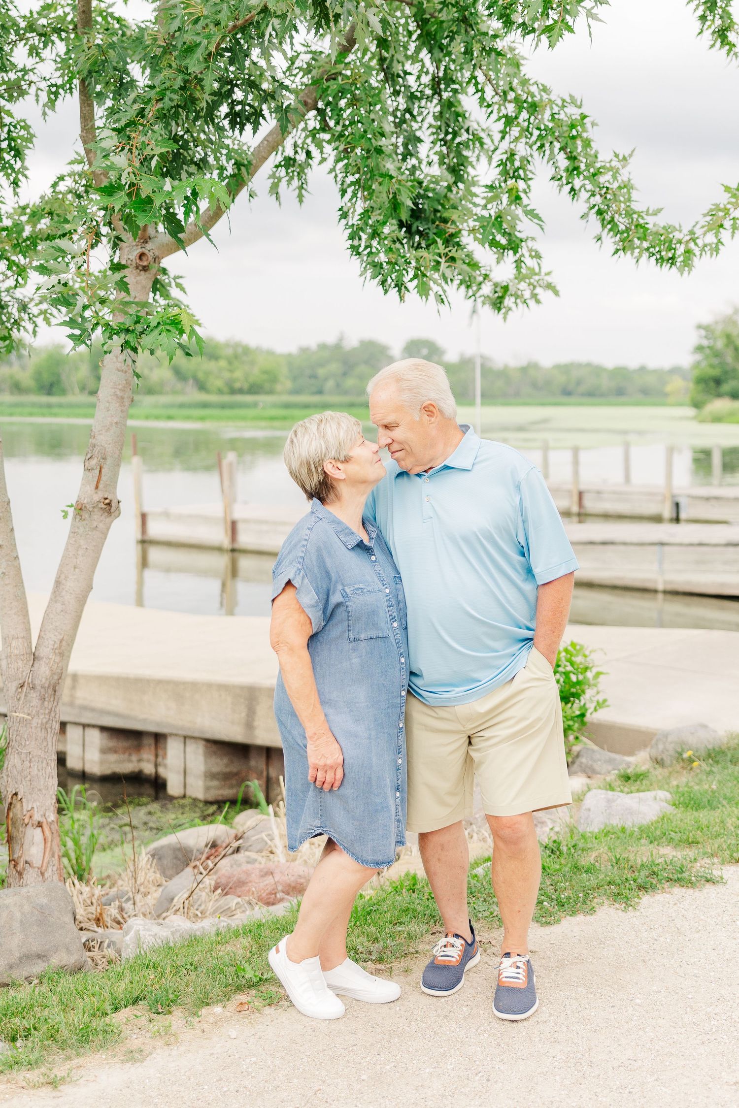 Elderly couple enjoying a tender moment while standing on a path near a lake and dock.