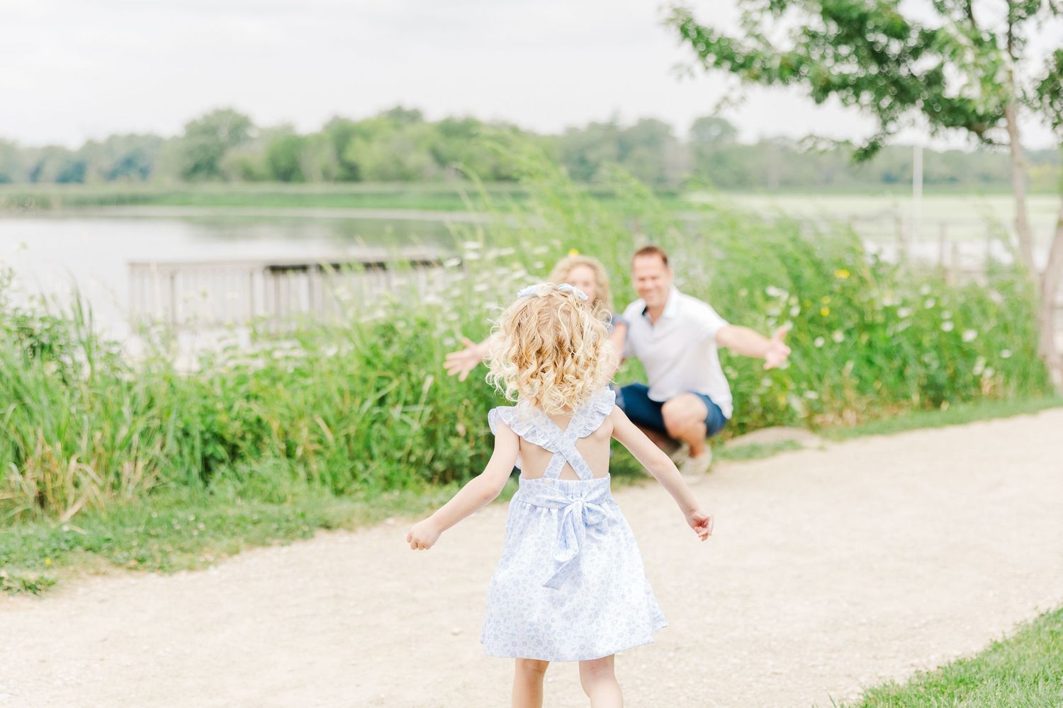 A joyful child runs along a lakeside path while wearing a light blue dress on a sunny summer day.