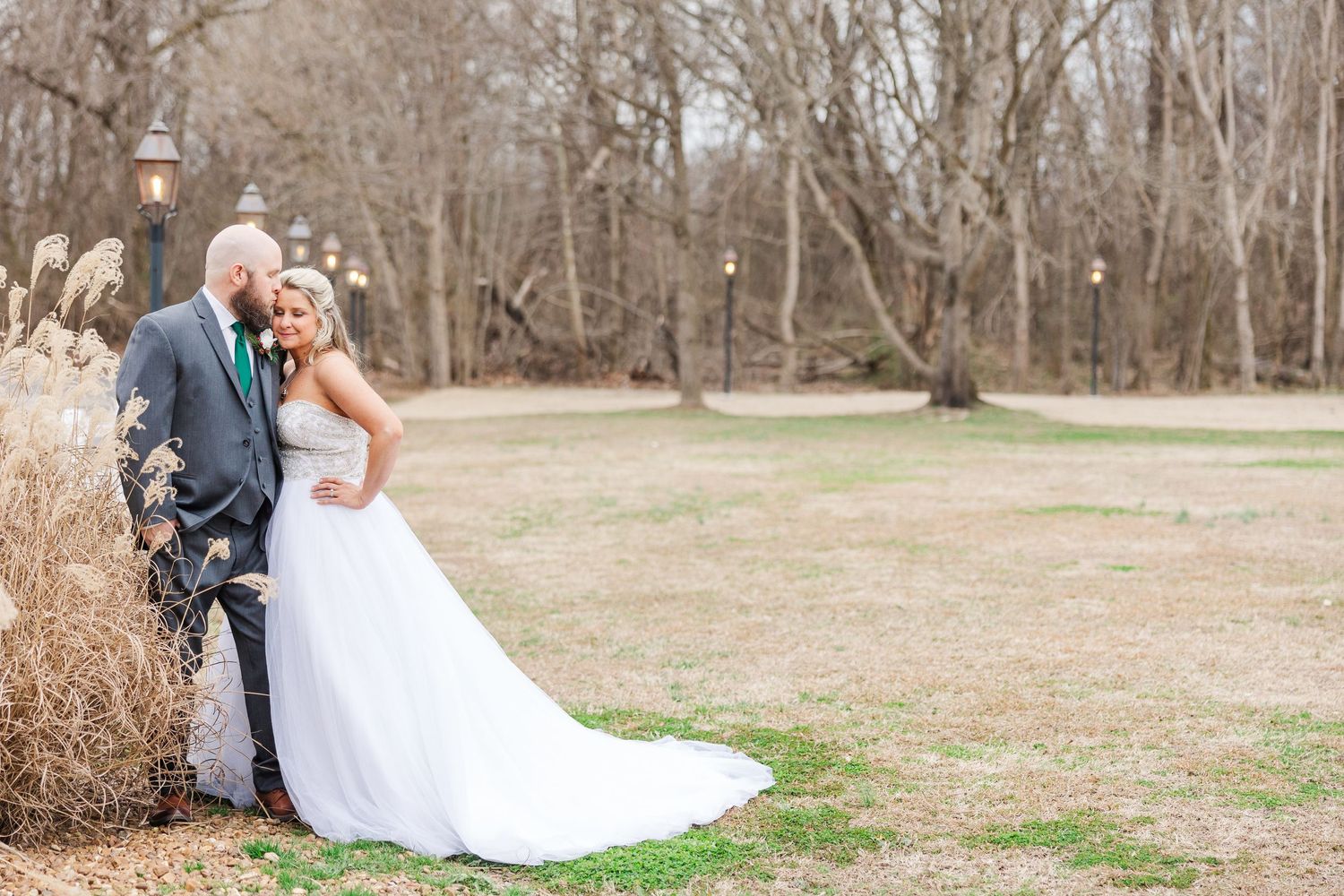 Newlyweds share a romantic moment on their wedding day surrounded by winter trees and dried grasses.