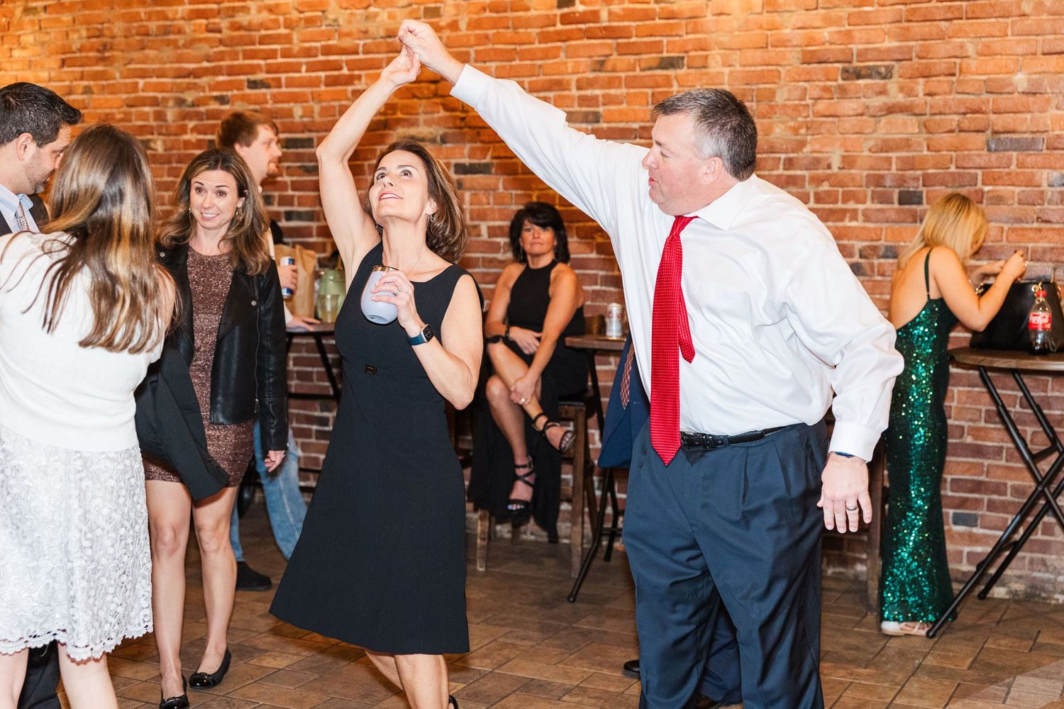 Wedding guests enjoying a lively dance at a reception with brick walls and festive atmosphere.