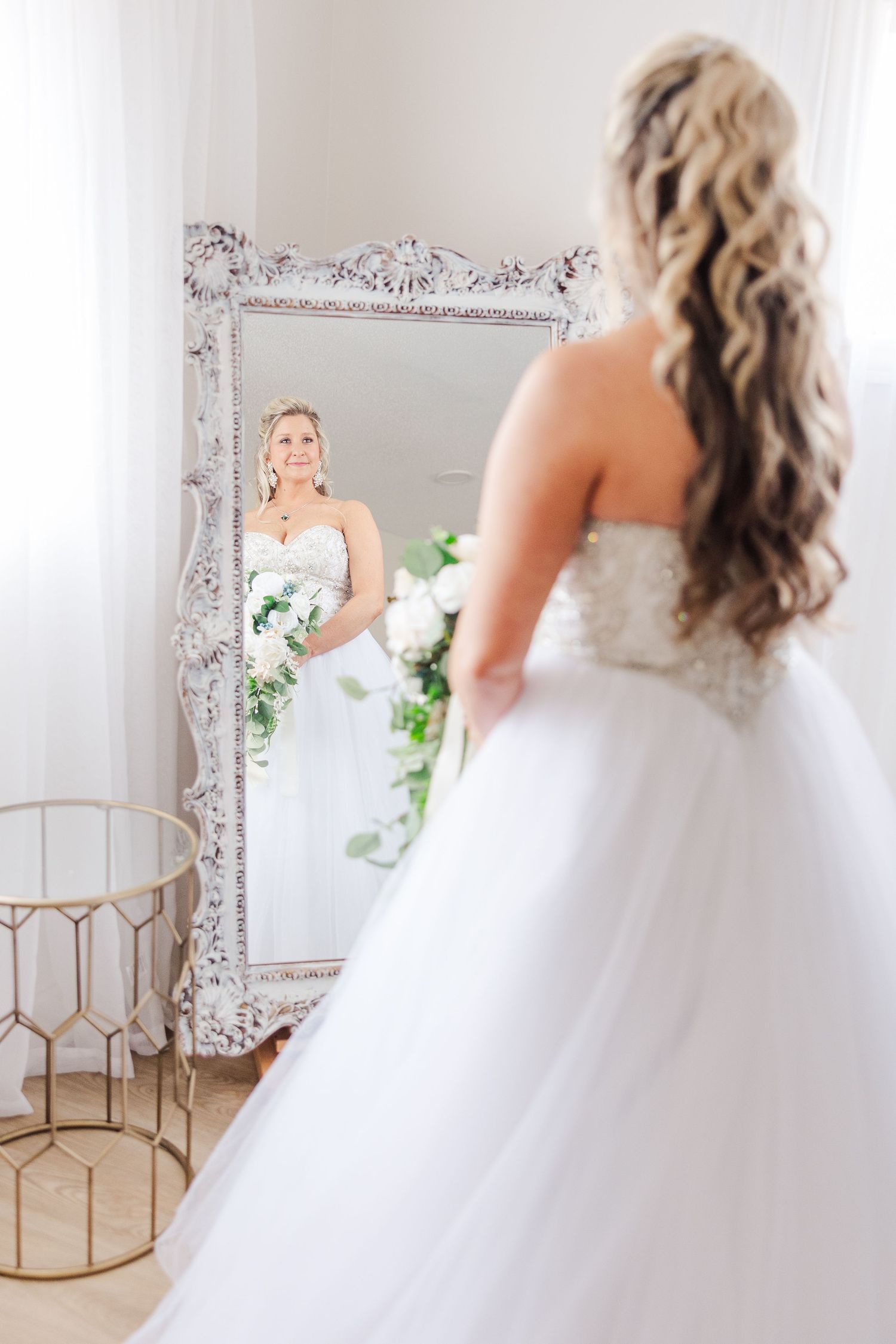 Beautiful wedding dress reflection in an ornate vintage mirror with floral decorations.