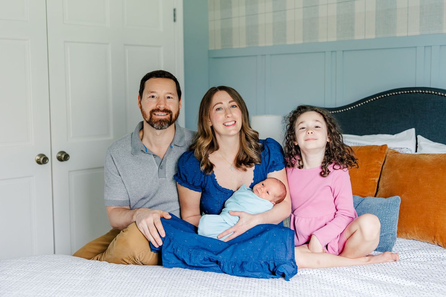 Family of four smiling on bed during in-home lifestyle newborn session in Crystal Lake, Illinois
