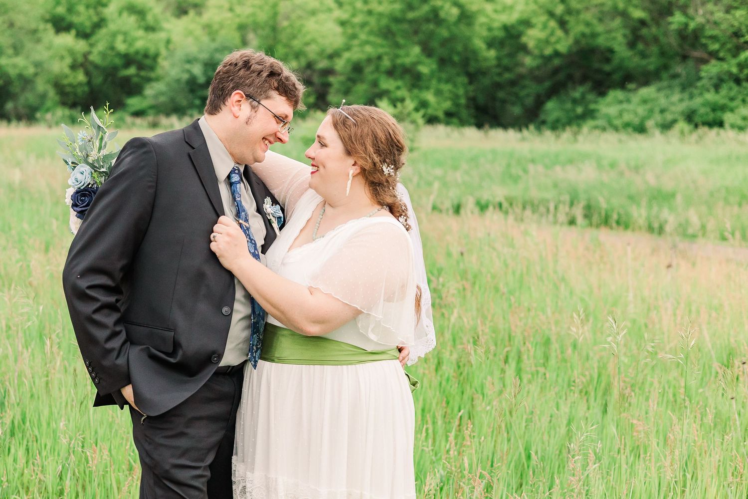 A romantic spring wedding photo of a couple sharing a moment in a green meadow.