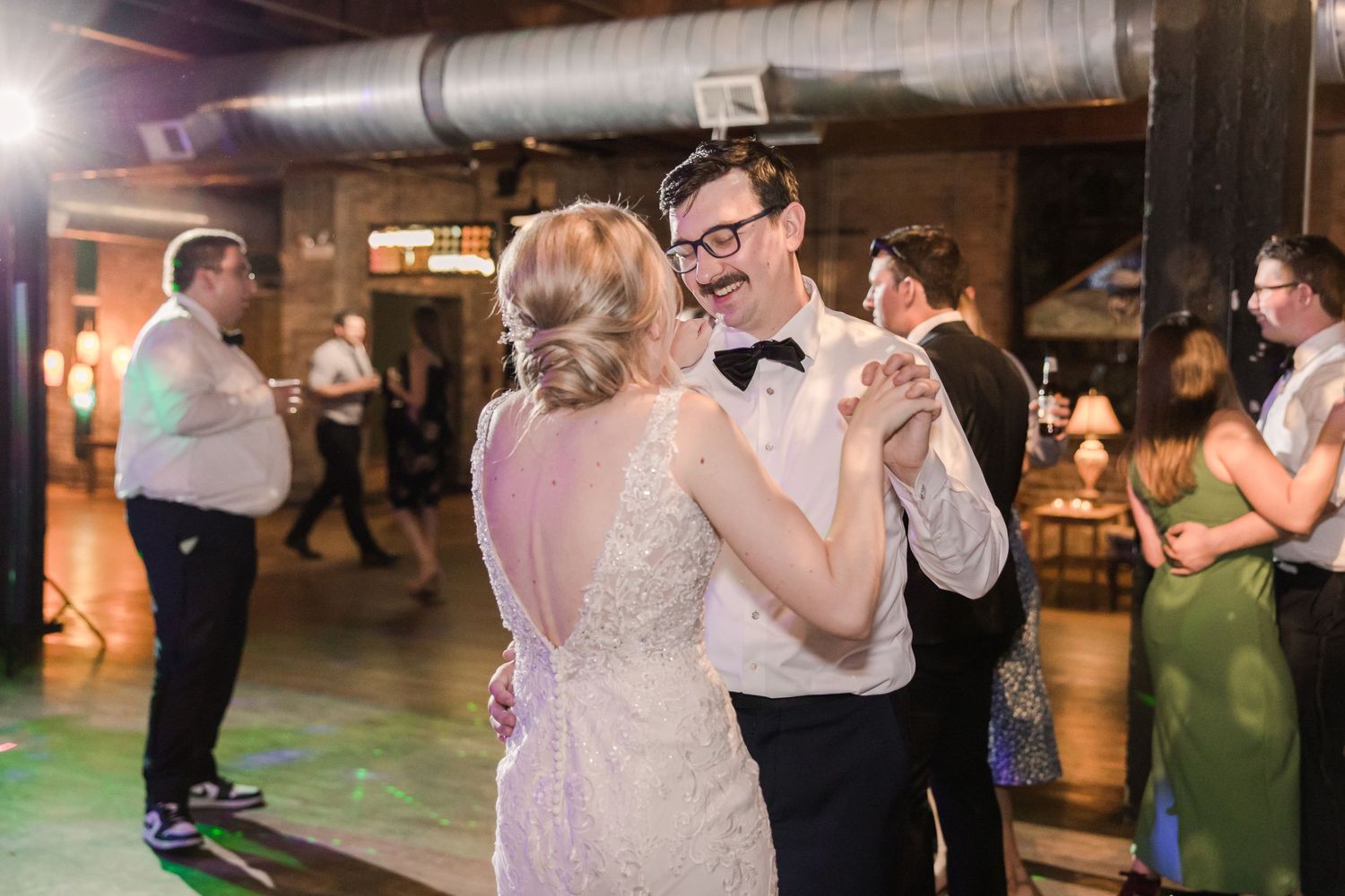 A couple shares a dance together at their wedding reception in an industrial-style venue.