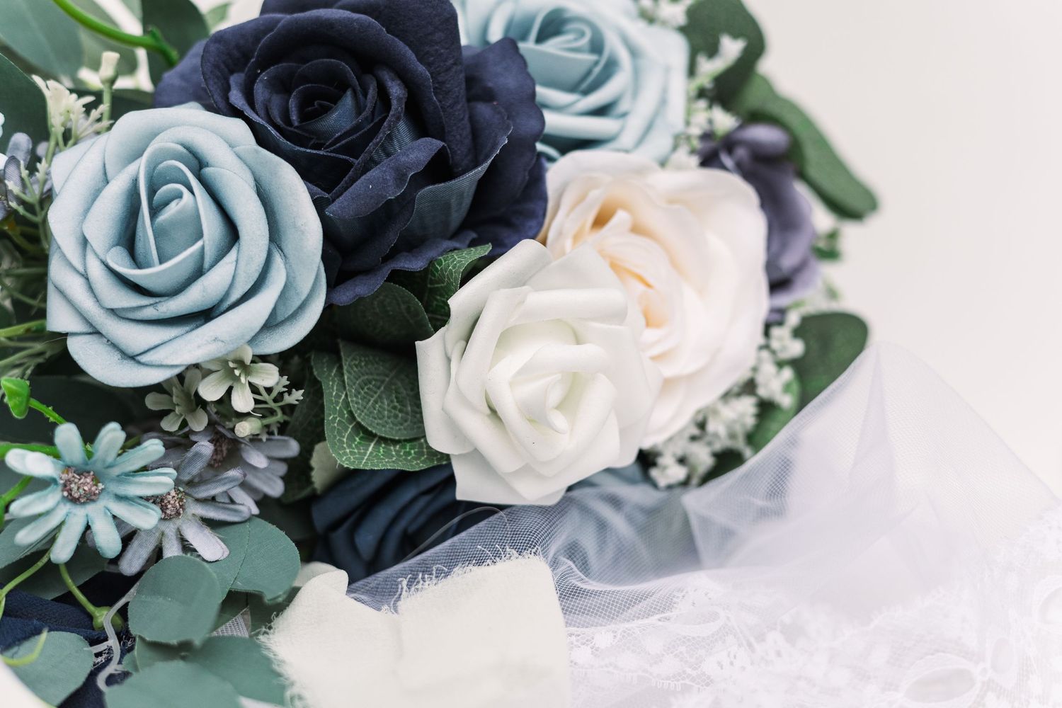 Wedding bouquet featuring navy, light blue, and white roses with greenery.