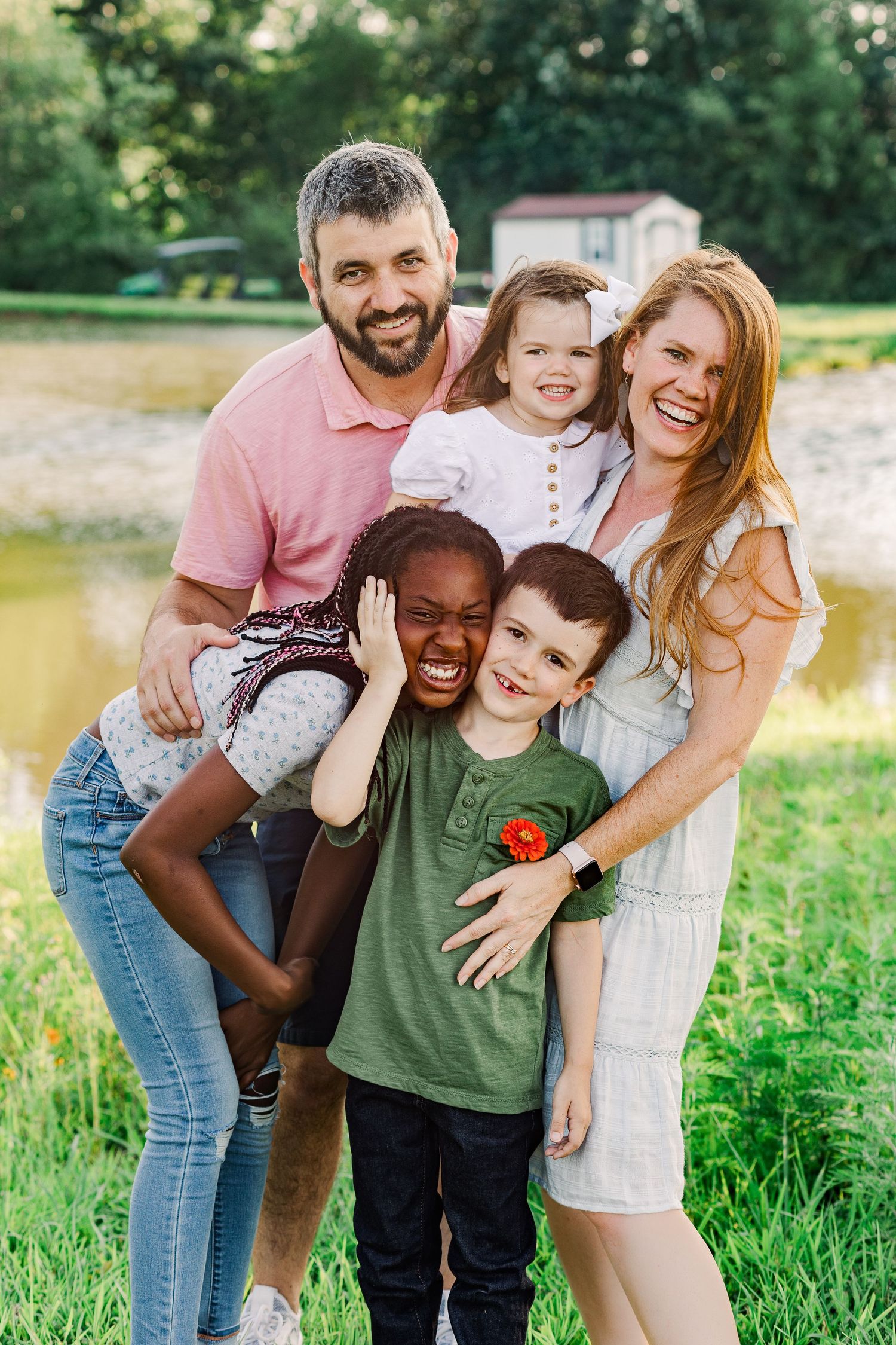 Family sharing playful moment together during outdoor photo session near pond.