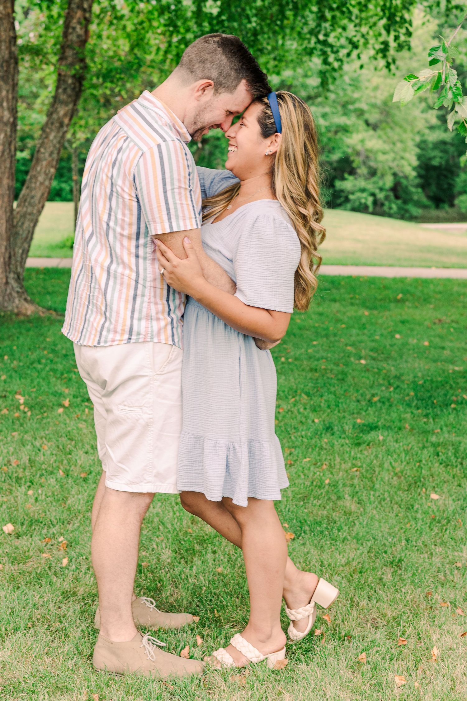 A couple shares an intimate moment while standing close together in a sunlit park setting.