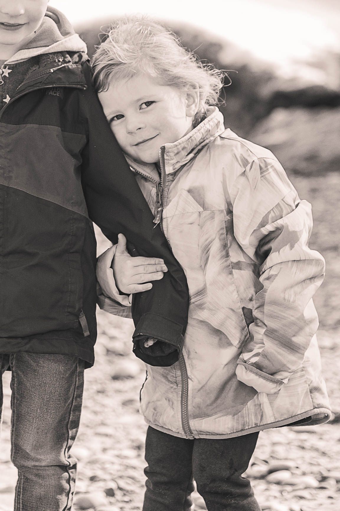 Black and white portrait of child in winter jacket on rocky beach.