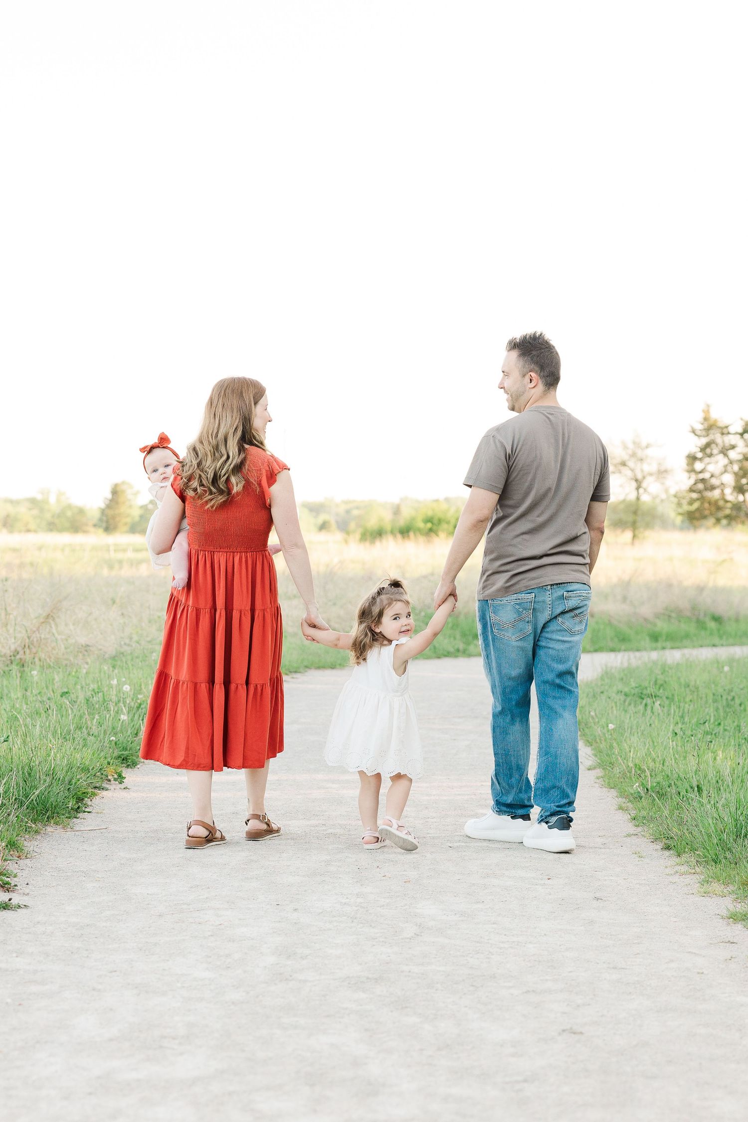 A family walks hand in hand down a dirt path during golden hour.