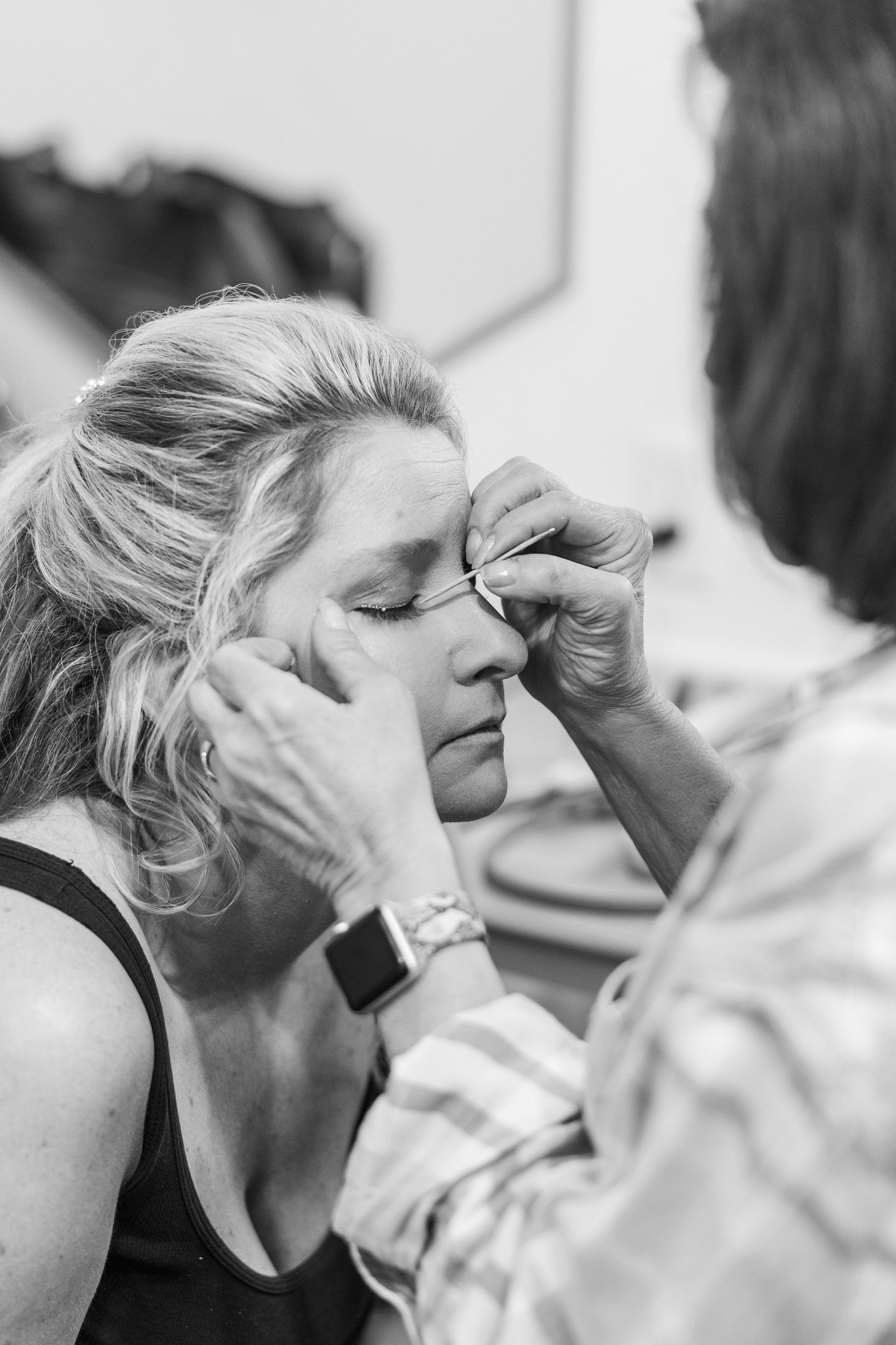 A makeup artist applying cosmetics to someone's face in black and white.