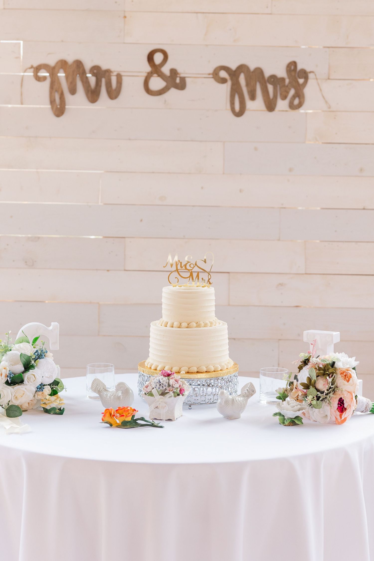 Two-tier white wedding cake with Mr & Mrs sign and floral decorations.