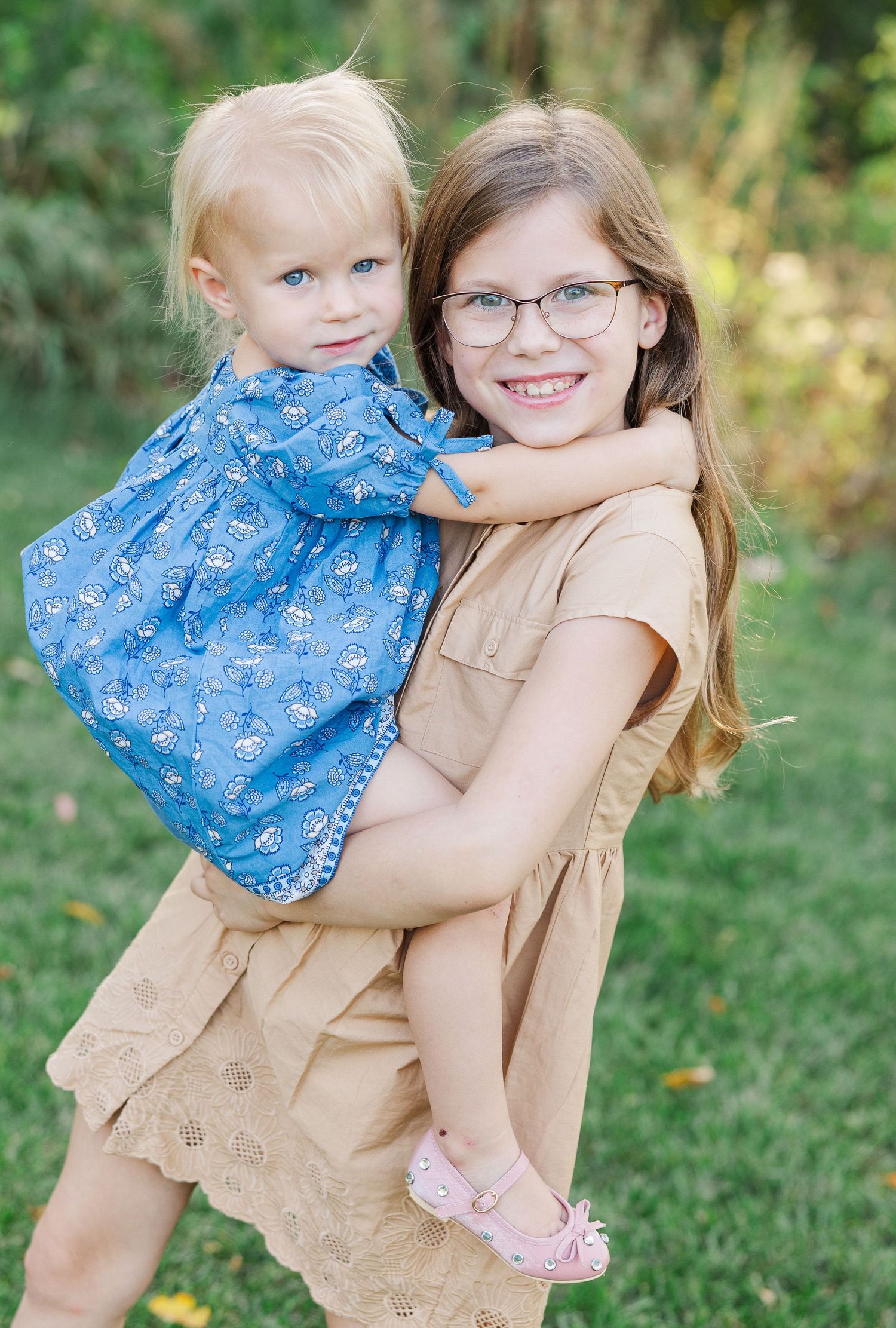 Two people in coordinating blue and beige outfits share sweet embraces while posing outdoors in a grassy setting.
