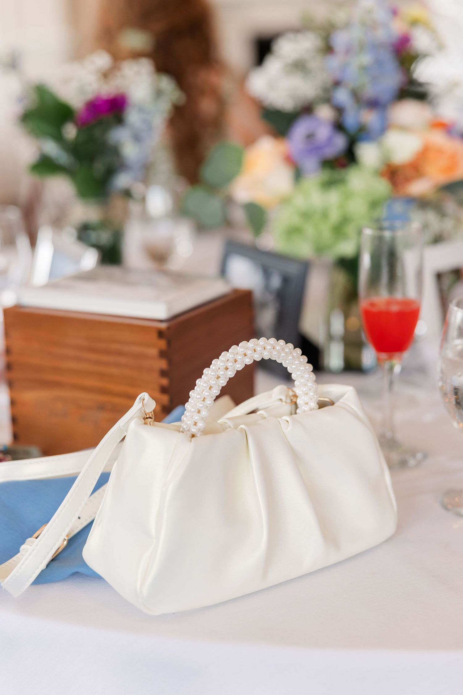 White pearl-handled bridal clutch purse on a table with floral centerpiece at a wedding.