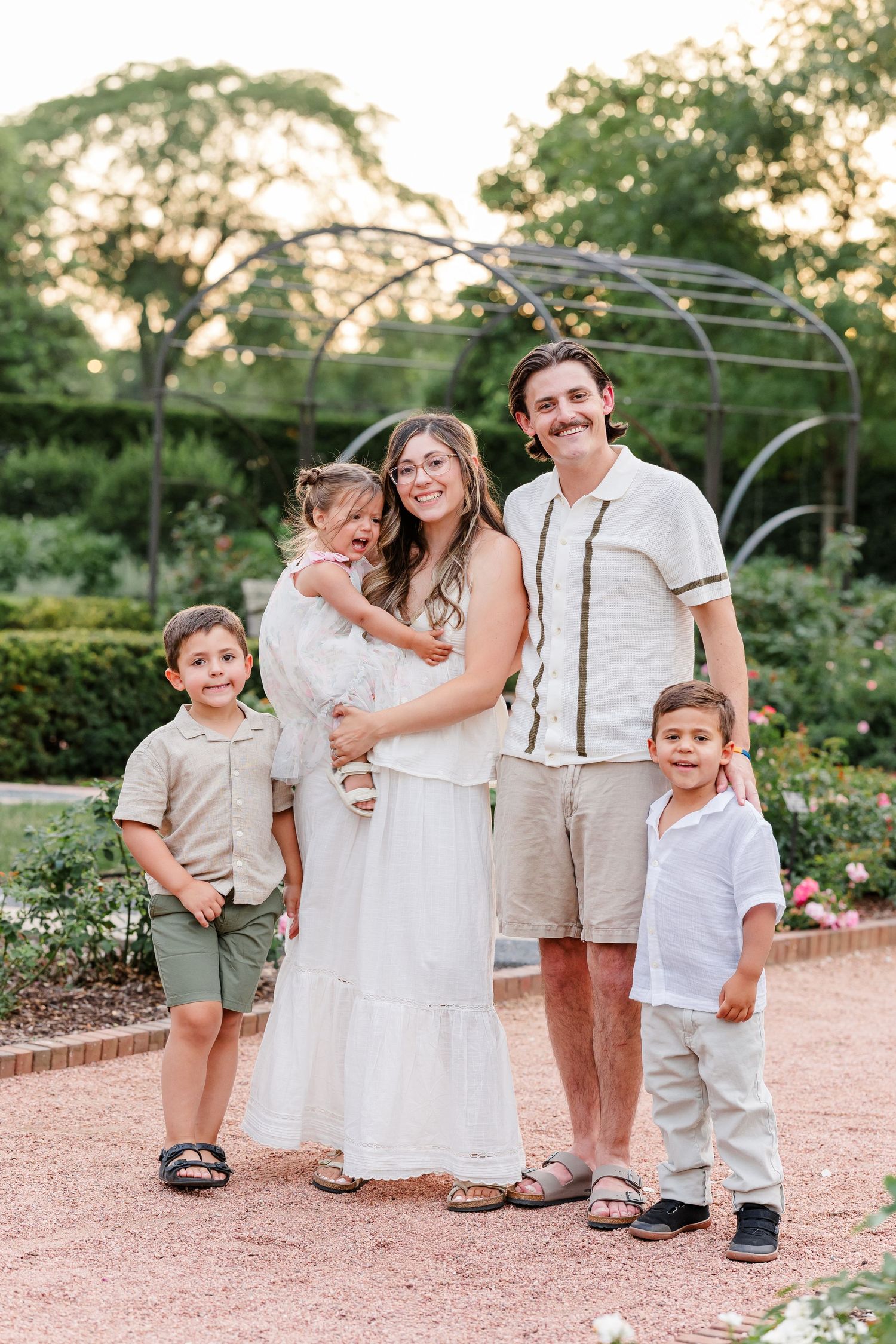 A family of five in neutral tones poses together in a beautiful garden at golden hour.