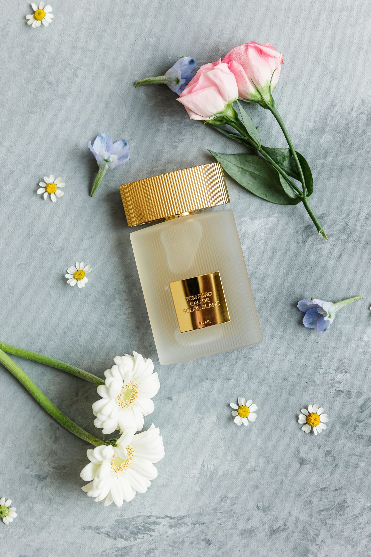 Tom Ford perfume bottle with pink roses, white daisies, and blue flowers on gray surface.