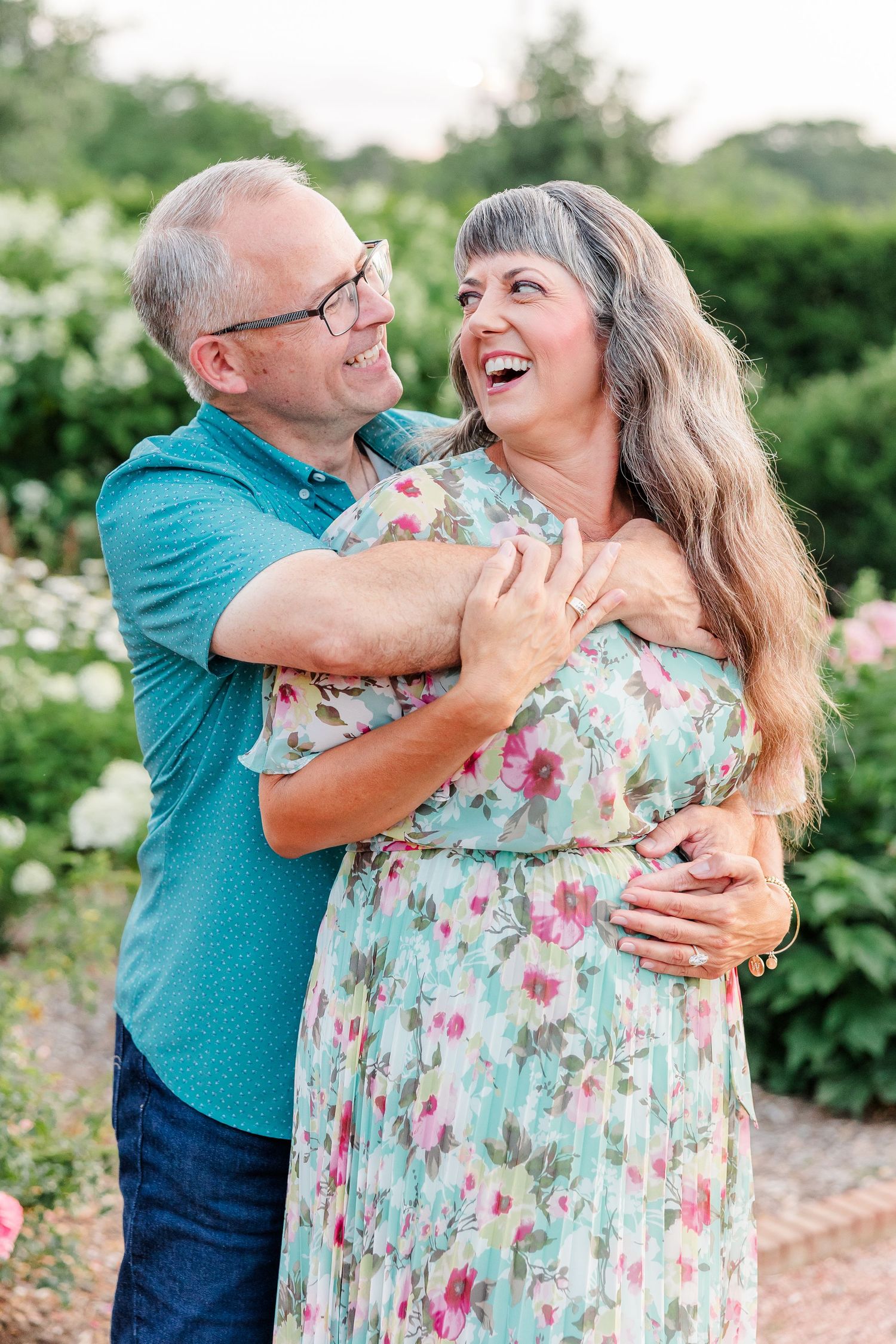 Happy middle-aged couple embracing and laughing together in a blooming rose garden.