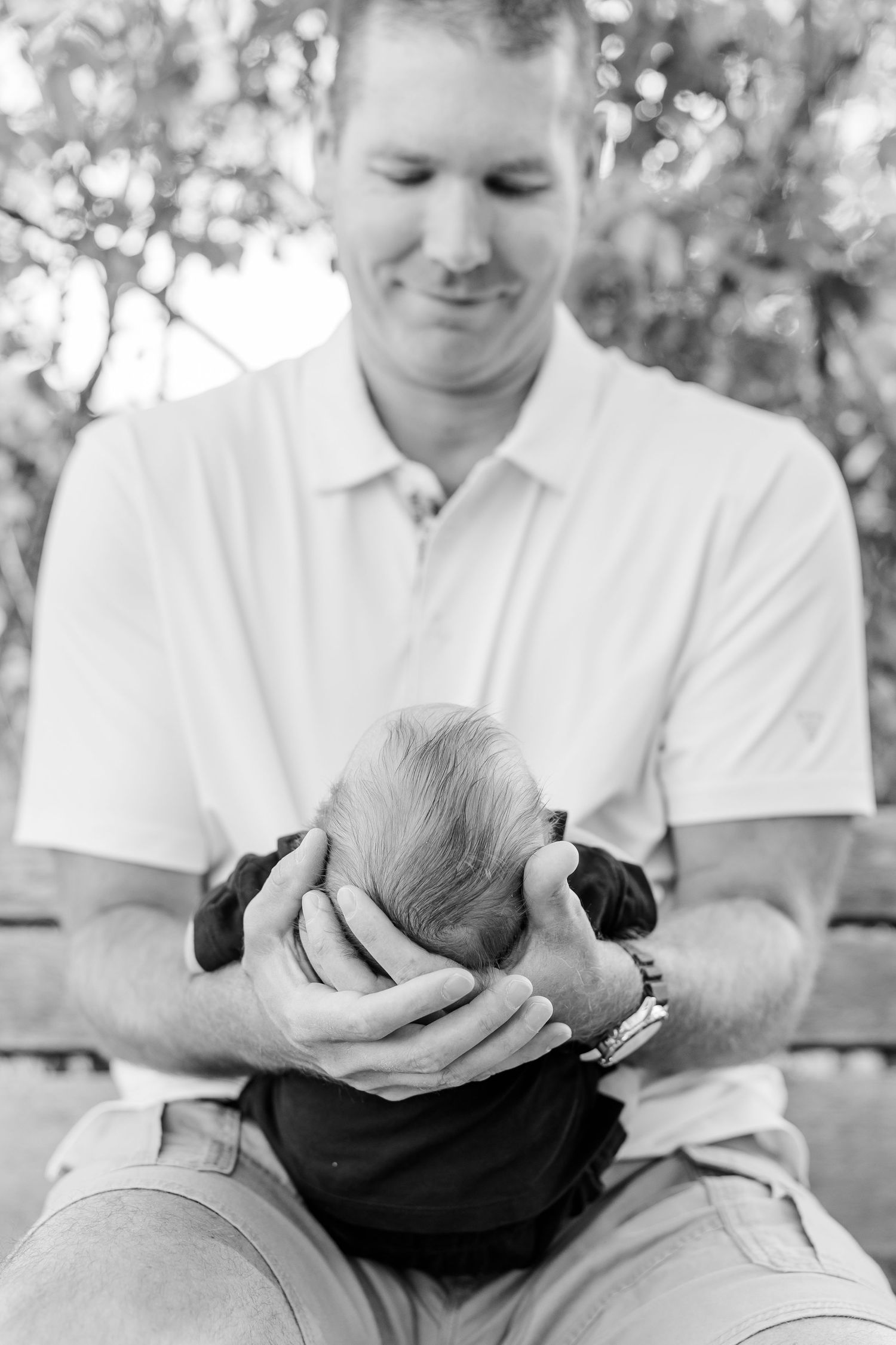 Black-and-white portrait of Andrew gently cradling newborn Lincoln in his hands.