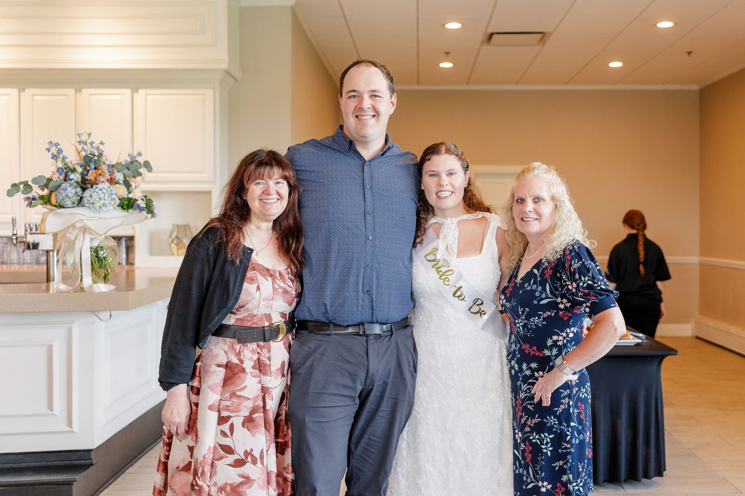 Bride-to-be wearing sash poses with three guests at an elegant bridal shower venue.