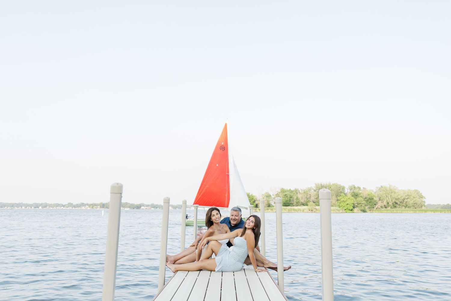 Family sitting on dock with sailboat during Pistakee Lake family photos in Johnsburg, Illinois