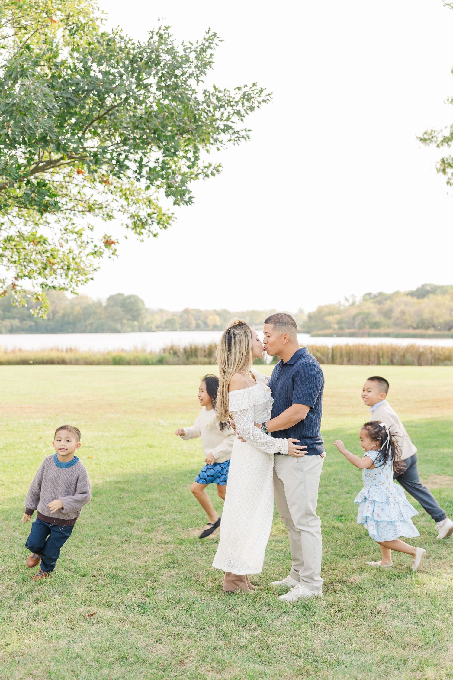 A couple shares drinks while children play and run around them in a sunny field near a lake during golden hour. Busse Woods