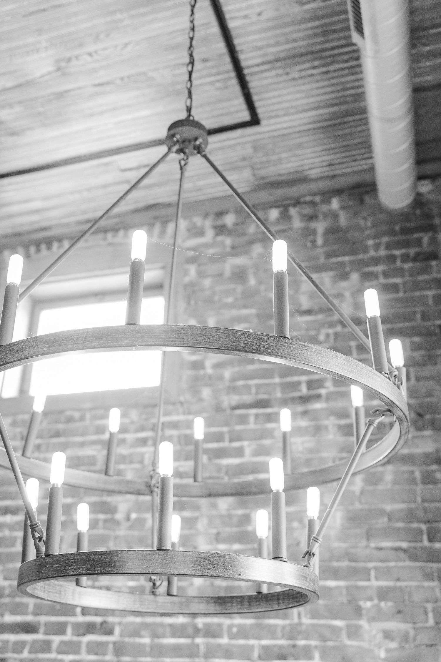 Industrial-style circular chandelier with exposed bulbs hanging against brick wall.