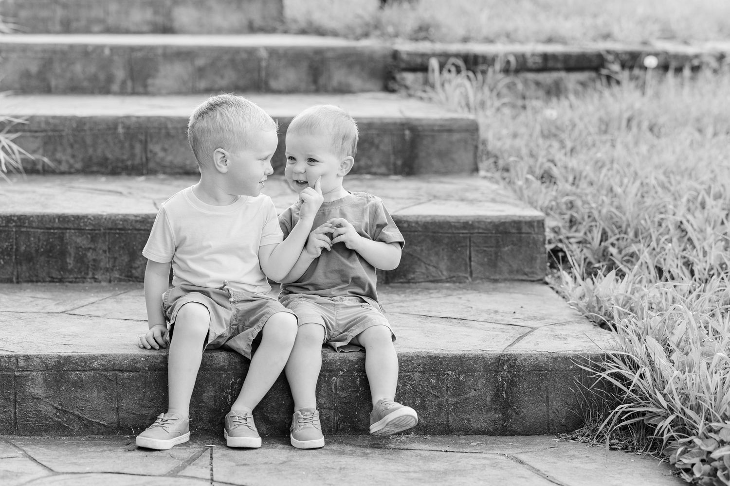Two small children sit together on outdoor stone steps in a sweet black and white portrait.