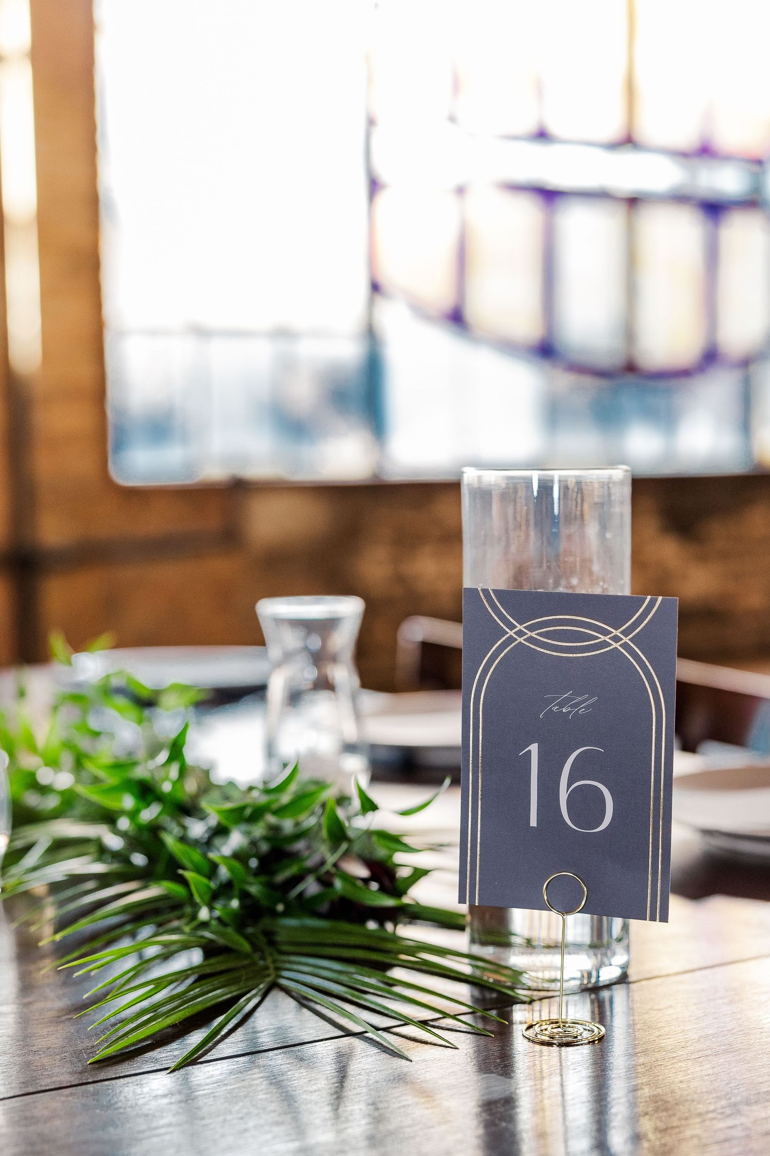 Rustic table setting with table number 16 and fresh greenery decor at an event venue.