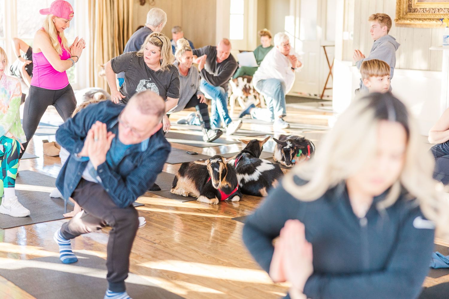 Group fitness class participants exercising together in a bright studio with wood floors.