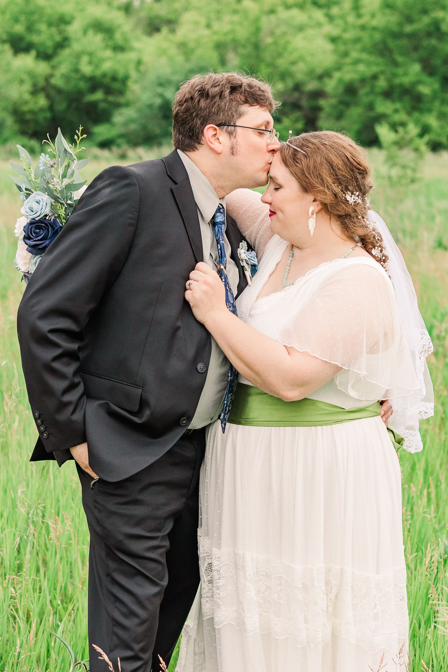 Romantic moment between newlyweds in a sun-lit meadow during their wedding photoshoot.