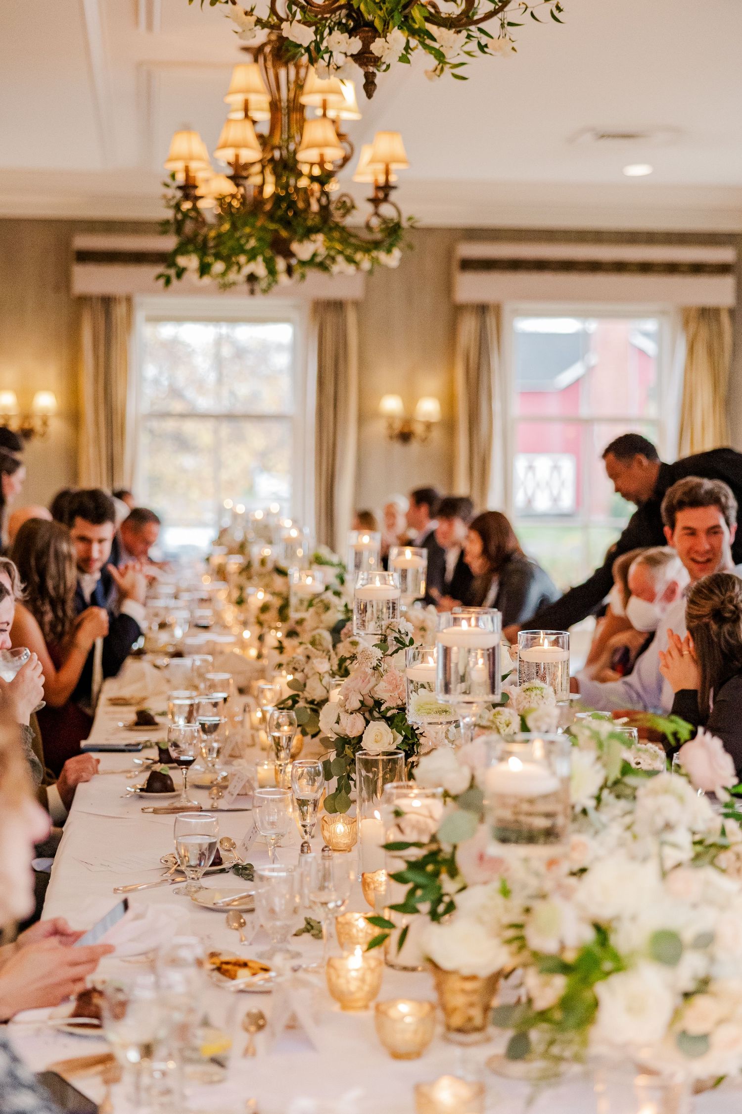 An elegant wedding reception table with candlelight, floral centerpieces and guests enjoying dinner.