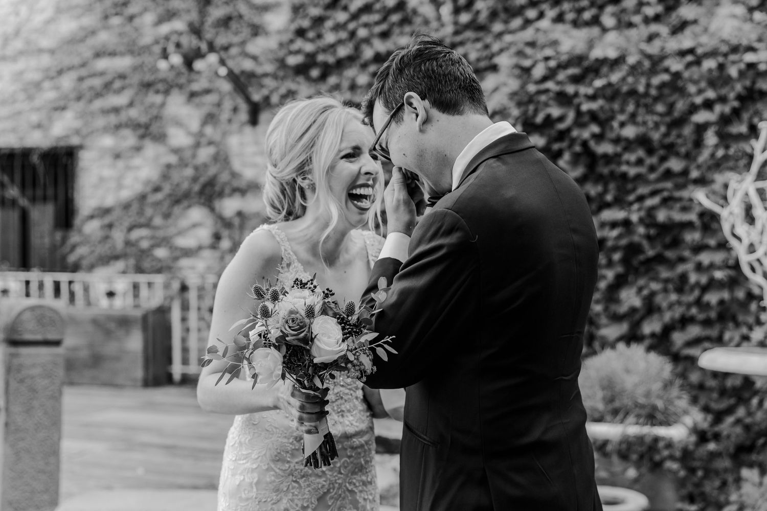 Black and white capture of couple sharing laughter during wedding first look.