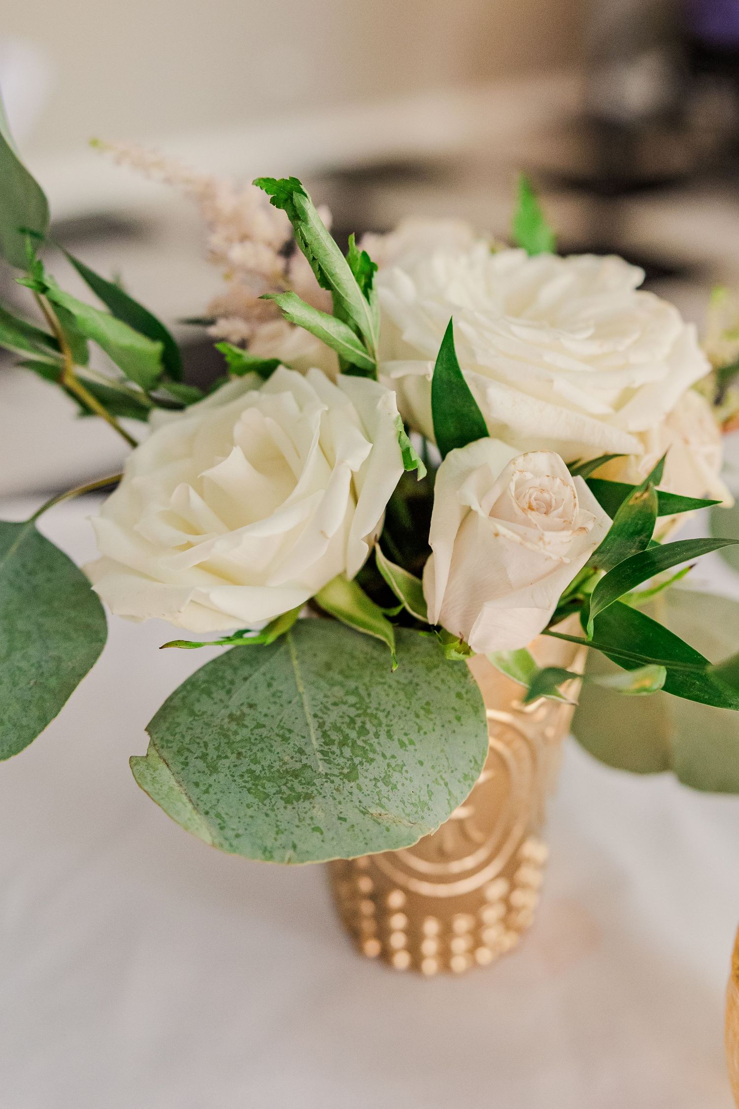 Elegant white roses and eucalyptus arrangement in textured gold vase.